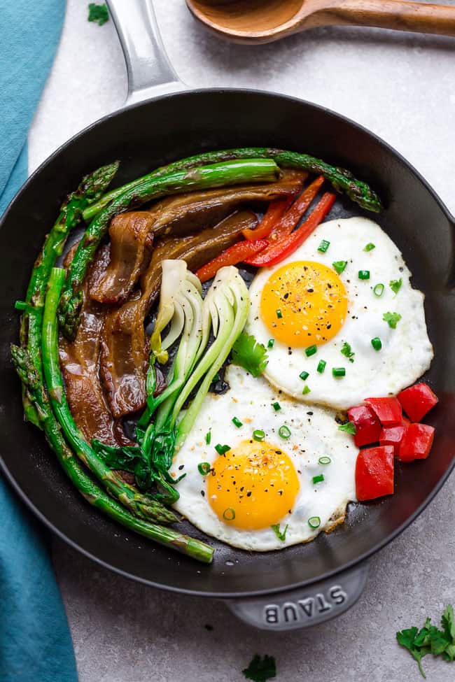 Top view of a skillet with sunny side up eggs with bacon and vegetables