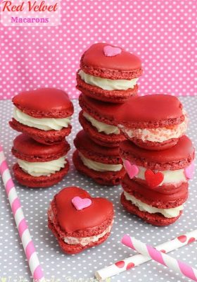 Eight red velvet macarons filled with cream cheese frosting stack on top of each other in three piles.