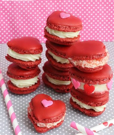 Eight red velvet macarons filled with cream cheese frosting stack on top of each other in three piles.