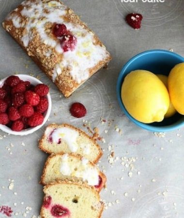Top view of Raspberry Lemon Loaf Cake with a few slices cut, fresh lemons, and fresh raspberries