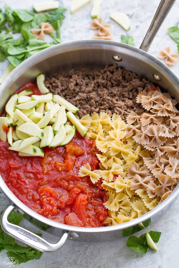 A pot with bowtie noodles, whole wheat bowtie noodles, cooked ground turkey, tomato sauce, diced tomatoes, and sliced zucchini, separated