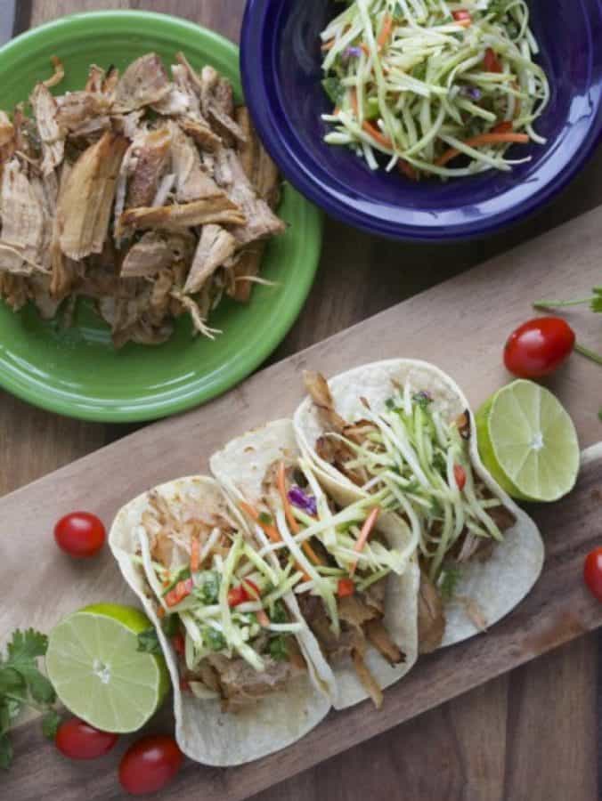 Overhead view of Jalapeno Ranch Carnitas tacos on a platter with a bowl of shredded carnitas and broccoli slaw