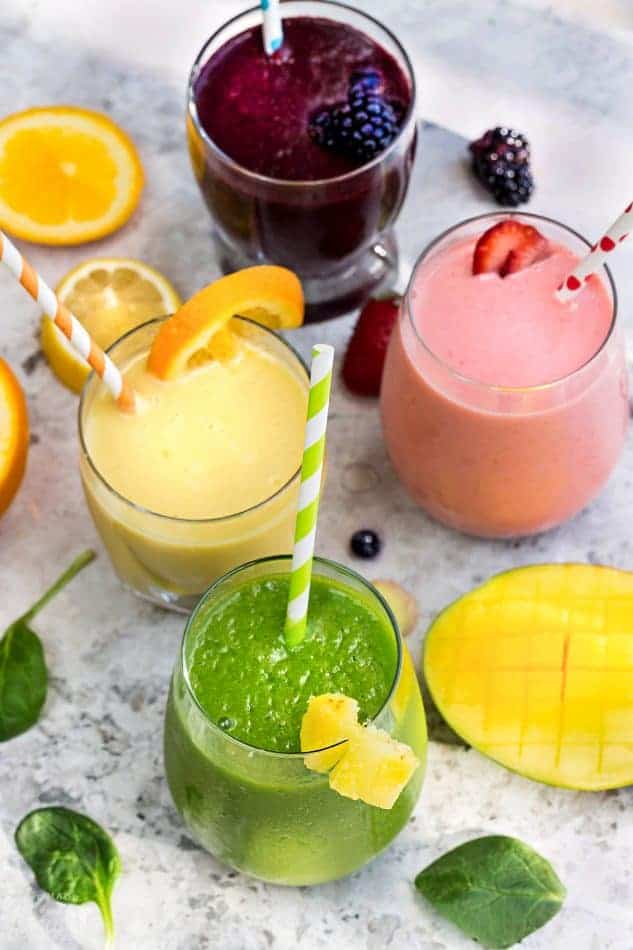 Top view of five healthy smoothie recipes in a clear glass with a straw on a grey marble background with fruit