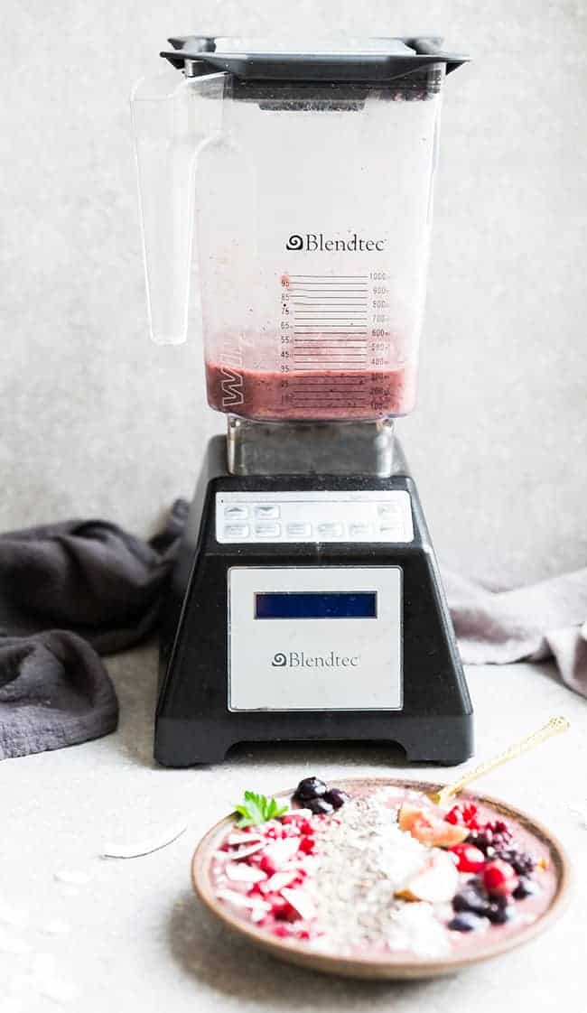 A Blendtec blender on a countertop with a kitchen towel behind it and a smoothie bowl in front of it