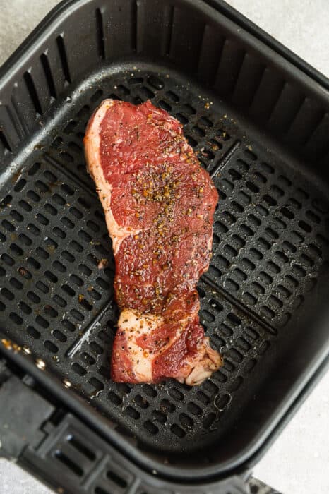 Top view of raw rib-eye steak in the air fryer basket