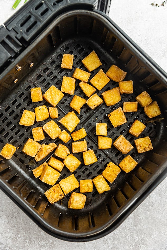 Cooked cubes of tofu in a single layer in an air fryer basket with plenty of space between each cube