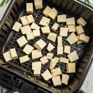 Uncooked cubes of extra-firm tofu inside of an air fryer basket
