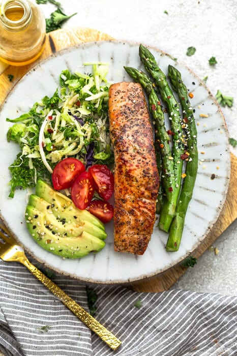 A plate of air fryer salmon on white plate with asparagus and salad