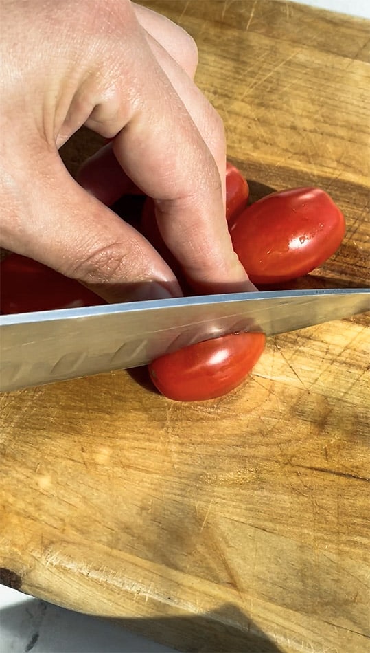 Close-up of cherry tomatoes being halved on a cutting board