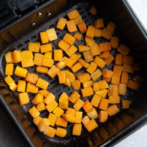 Top view of chopped raw butternut squash cubes in an air fryer basket