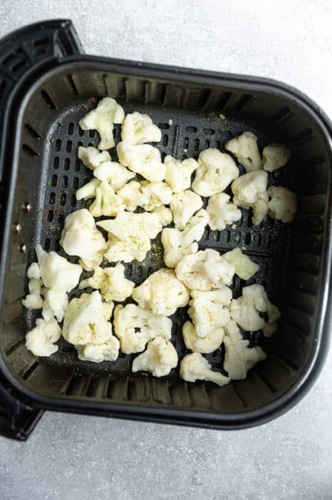 Top view of frozen cauliflower florets in an air fryer basket