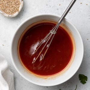 Sweet and spicy sauce in a white bowl with a whisk