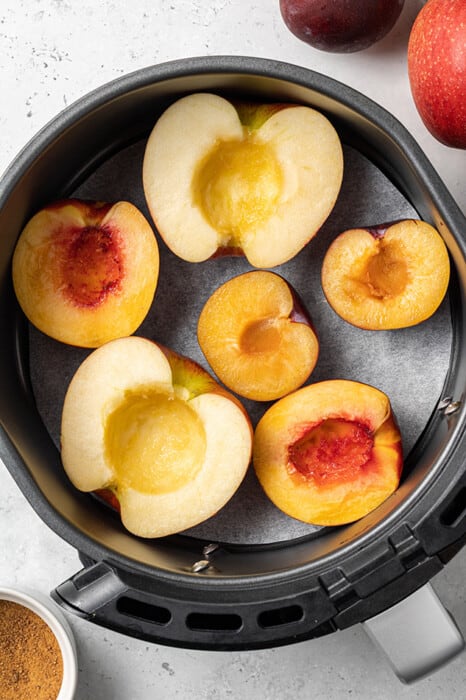 Overhead view of apple, peach and plum halves in an air fryer