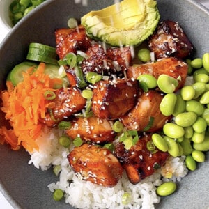A bowl of air fryer salmon bites over a bed of cooked jasmine rice, edamame, avocado, carrots and cucumber