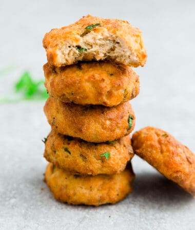 Side view of 5 stacked crispy salmon cakes one with a bite on a white background