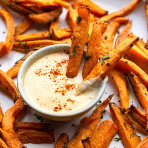 Side view of crispy air fried sweet potato fries on a white oval plate with creamy cashew dip