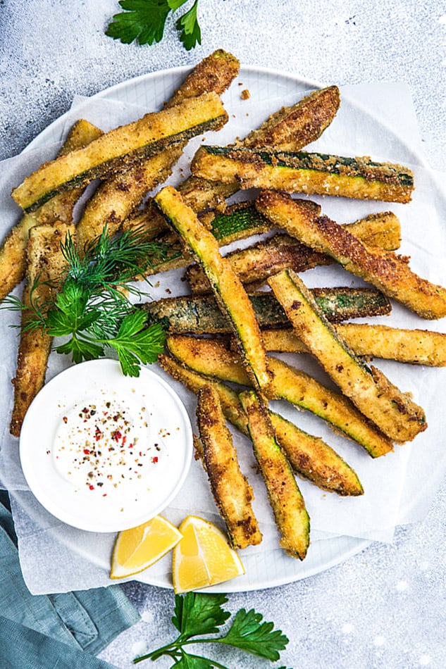 Top view of air fryer zucchini fries on a white plate with dip 