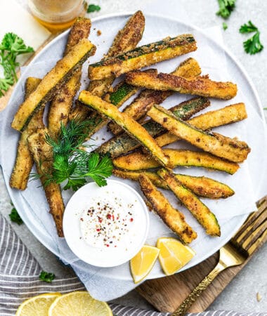 Top view of air fryer zucchini fries on a white plate with dip
