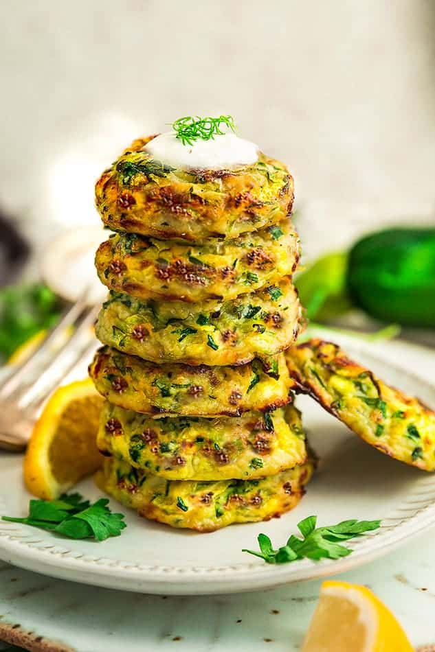 Side view of 6 stacked air fryer zucchini fritters on a white plate