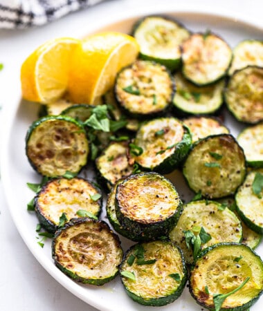 Side shot of air fryer zucchini rounds on a white plate