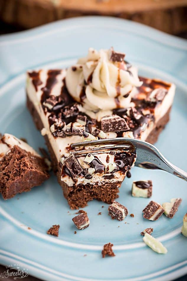 A slice of Mint Andes Chocolate Brownie Cheesecake on a plate with a fork cutting into it