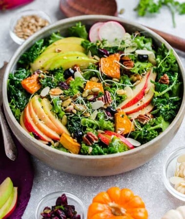 Side view of a apple fall salad with kale, butternut squash and apples in a white bowl with a gold fork on the side