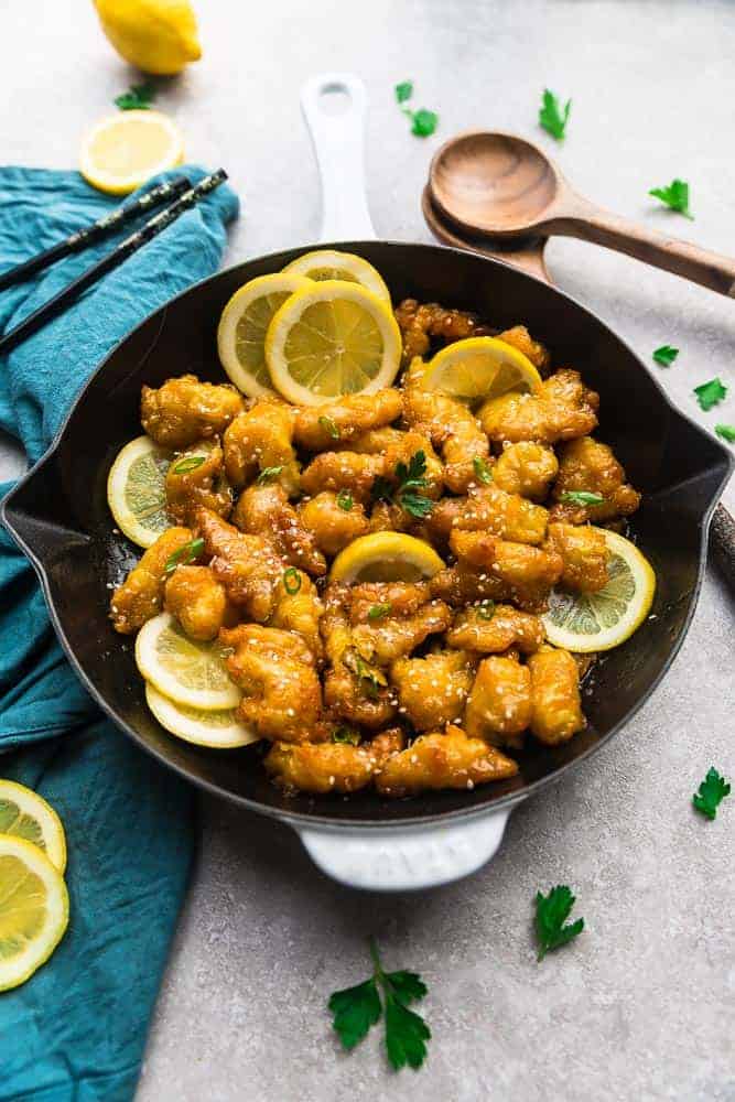 Overhead view of Asian lemon chicken in a skillet with lemon slices, surrounded by lemon slices, chopsticks, and wooden spoons