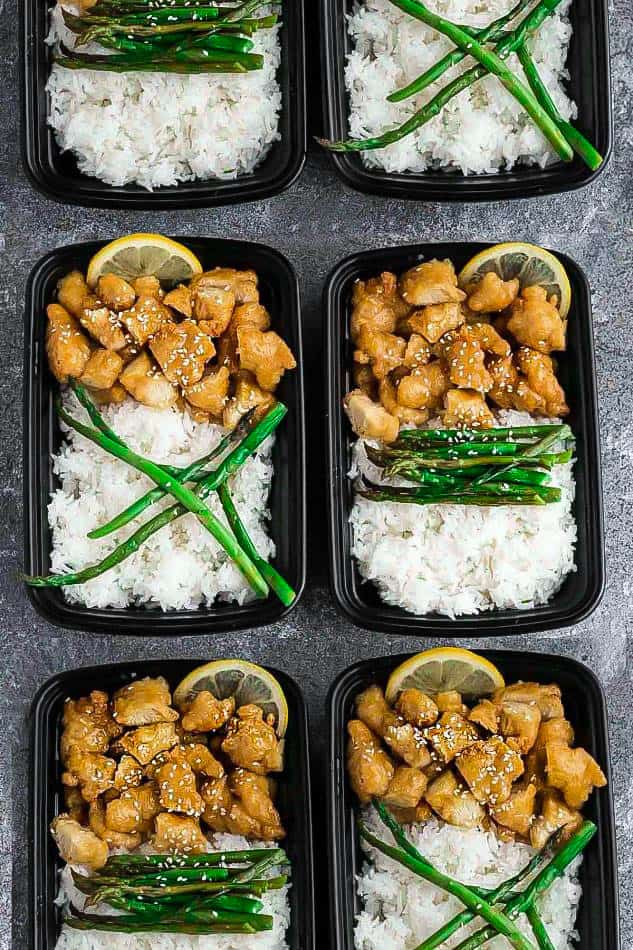 Top view of six meal prep containers of Asian honey lemon chicken with rice and asparagus and lemon slices