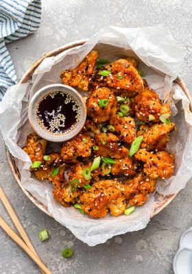 Top shot of a batch of crispy Asian Vegan Cauliflower wings served a savory dipping sauce in a white bowl
