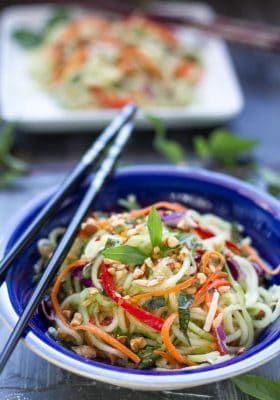 Top view of a serving of Zucchini noodle salad in a blue bowl with chopsticks on top