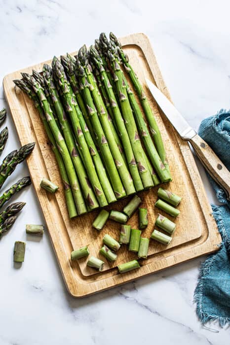 Top view of uncooked asparagus spears on a wooden cutting board with a knife