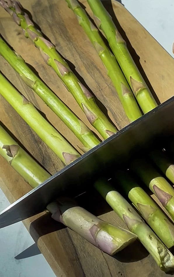 Close-up of a chef's knife trimming fresh asparagus spears