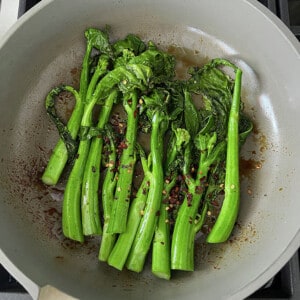 A bunch of stir-fried Chinese broccoli (Gai Lan) in a grey pan with chili flakes