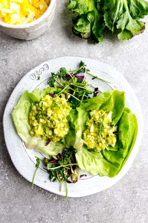 Two big scoops of avocado egg salad in two lettuce wraps sitting side by side on a white plate