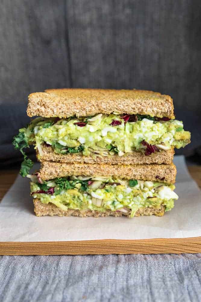 Two halves of an egg salad sandwich stacked on a parchment-lined cutting board