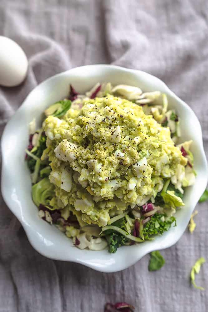 An avocado egg salad in a white bowl on top of a tan kitchen towel