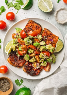 Overhead shot of air fryer salmon topped with avocado salsa on a white plate