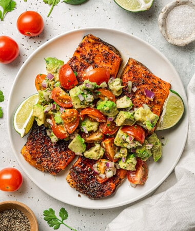 Overhead shot of air fryer salmon topped with avocado salsa on a white plate