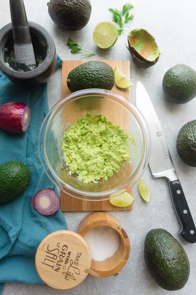 Overhead view of Homemade Guacamole in a glass bowl surrounded by ingredients