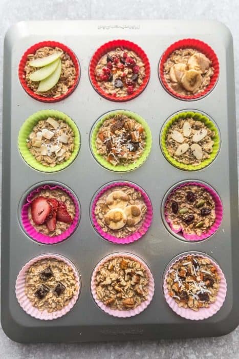 Twelve Unbaked Oatmeal Cups with Different Toppings in a Muffin Tin