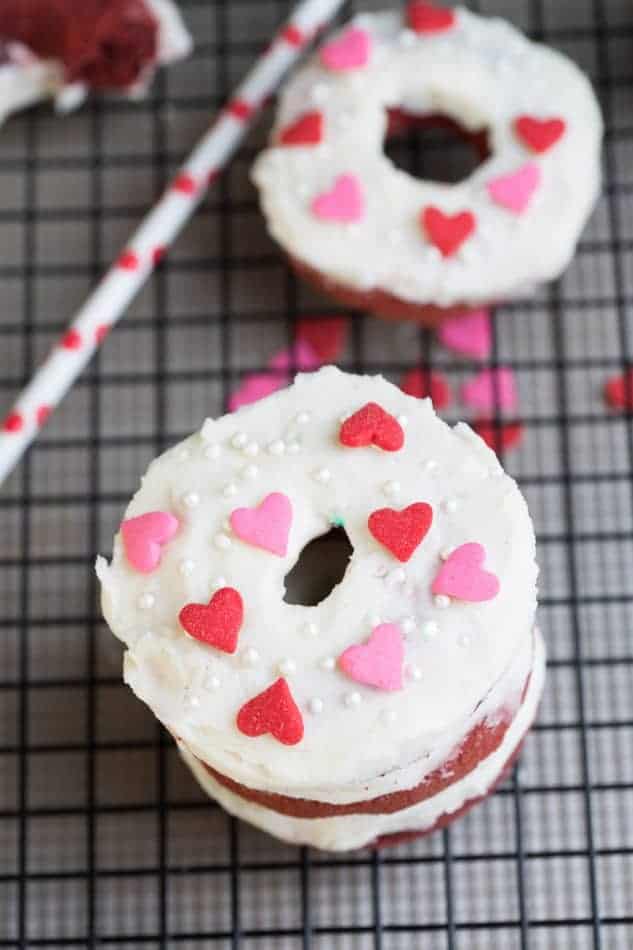 Baked Red Velvet Cake Donuts with Cream Cheese Glaze and heart shaped sprinkles stacked on a cooling rack