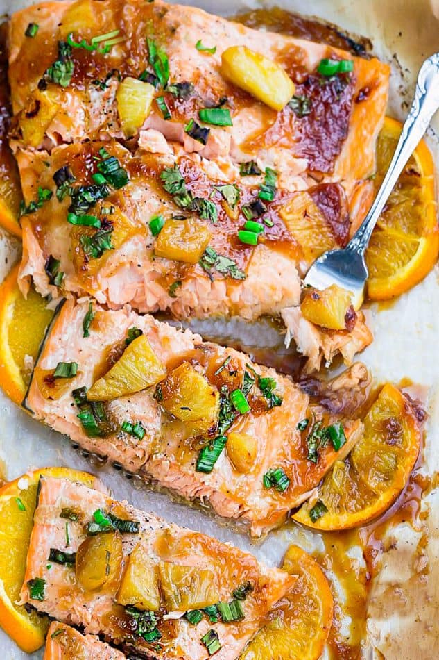Four Pineapple Orange Teriyaki Glazed Salmon Fillets with Orange Slices on a Piece of Parchment Paper
