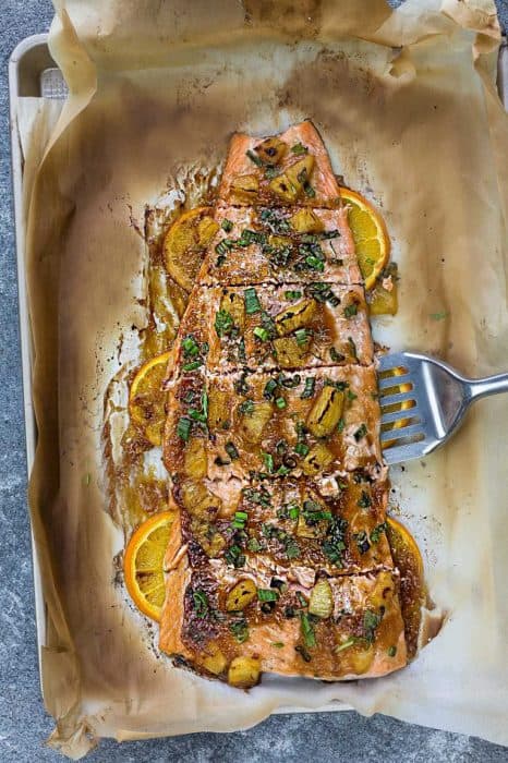 Six Baked Salmon Fillets on a Pan with Orange Slices Slid Halfway Underneath Them