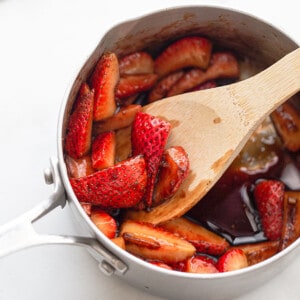 Sliced strawberries with balsamic vinegar and maple syrup in a stainless steel pot with a wooden spoon