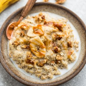 A bowl of banana oatmeal topped with banana slices, date caramel, walnuts and a splash of milk