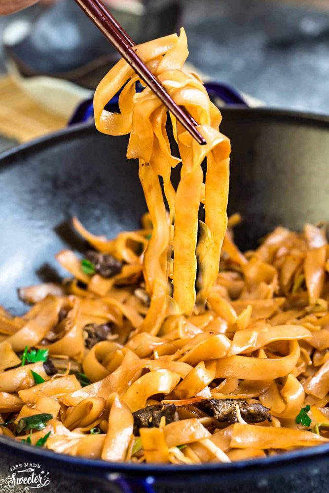 Simple Fried Ho Fun Noodles being scooped out of a black dish with red chopsticks.