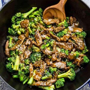 Top view of Whole30 beef stir fry in a blue cast-iron wok with a wooden spoon
