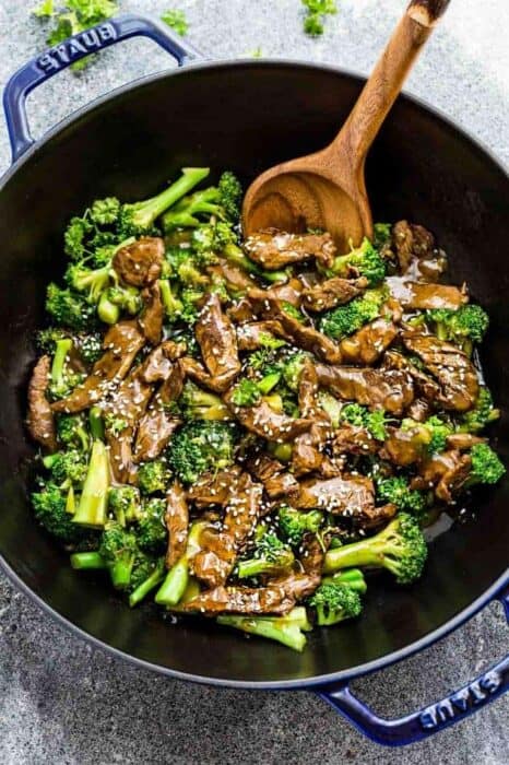 Top view of Whole30 beef stir fry in a blue cast-iron wok with a wooden spoon