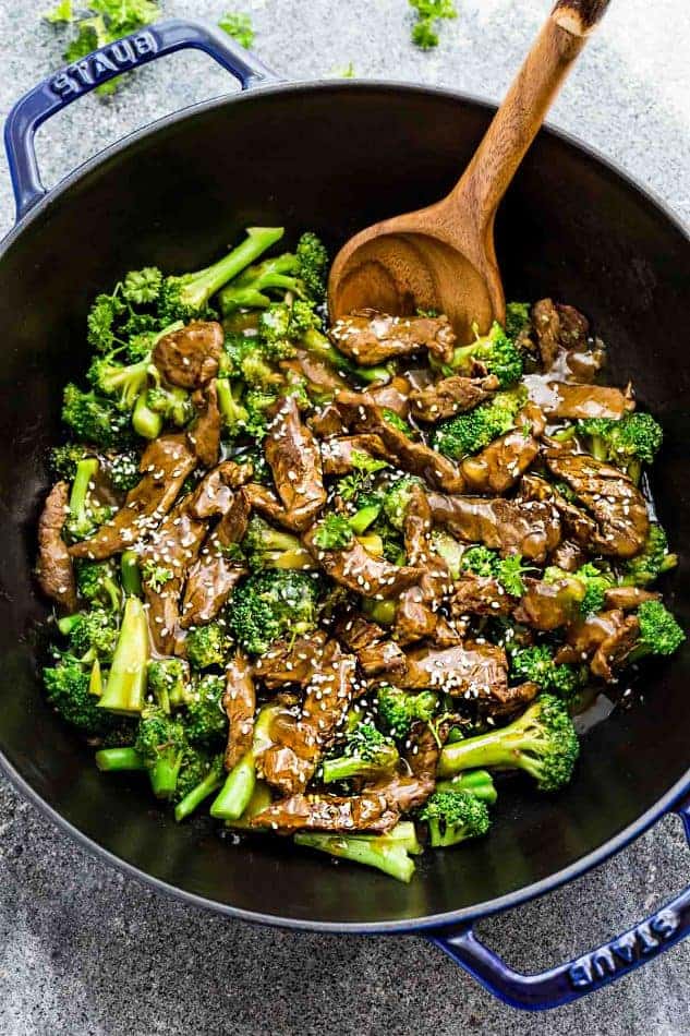 Skinny Beef and Broccoli Stir-Fry in a dark blue and black skillet with a wooden spoon.