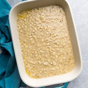 Oatmeal Breakfast Casserole Batter in a Tan and Teal Baking Dish Next to a Cloth Napkin